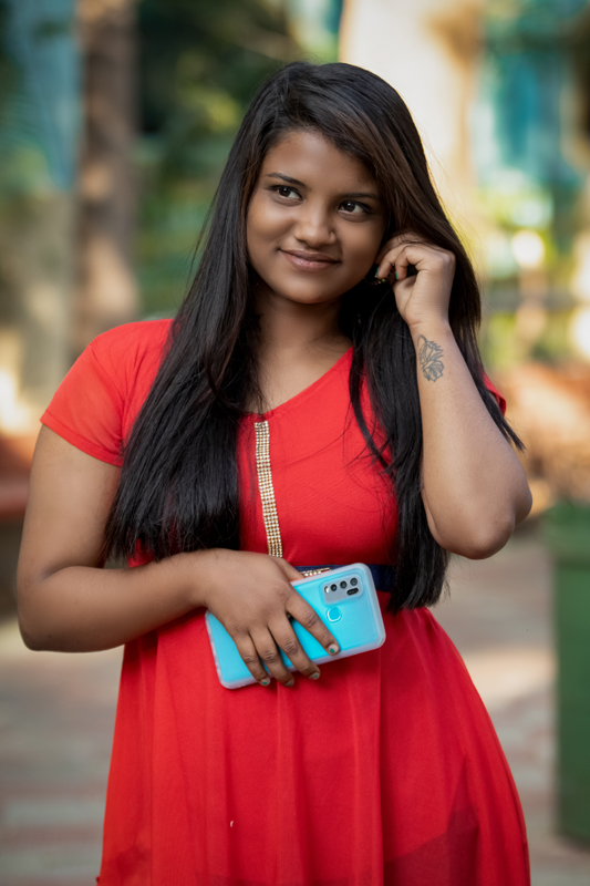 Photo of a woman with brown skin and long black hair, wearing a red dress, and holding a phone